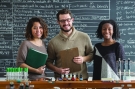 three students in front of a blackboard face a science lab